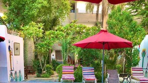 A swimming pool with a person swimming, surrounded by lounge chairs and a red umbrella. - Amon Hotel (Luxor)