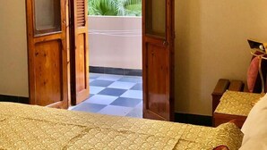 A room with a bed, a wooden door leading to a balcony, and a small table with a lamp. - Amon Hotel (Luxor)