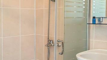 A glass-enclosed shower with a handheld showerhead and a wall-mounted faucet.