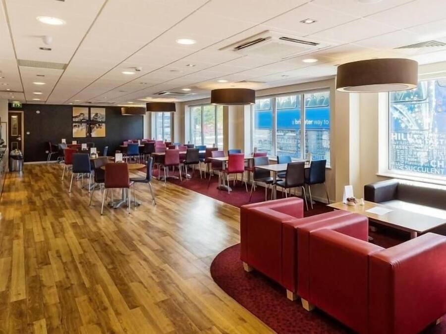 A modern restaurant with wooden flooring, red and black seating, and large windows offering a city view.