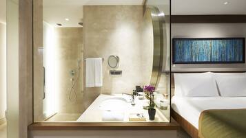 A modern hotel room with a large mirror, a sink, a shower, a bed, and a television.