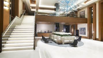 A modern hotel lobby with a central seating area, a staircase, and a large decorative ceiling piece.