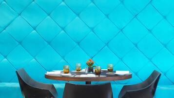 A round table with four chairs, a blue cushioned wall, and a small vase with flowers.