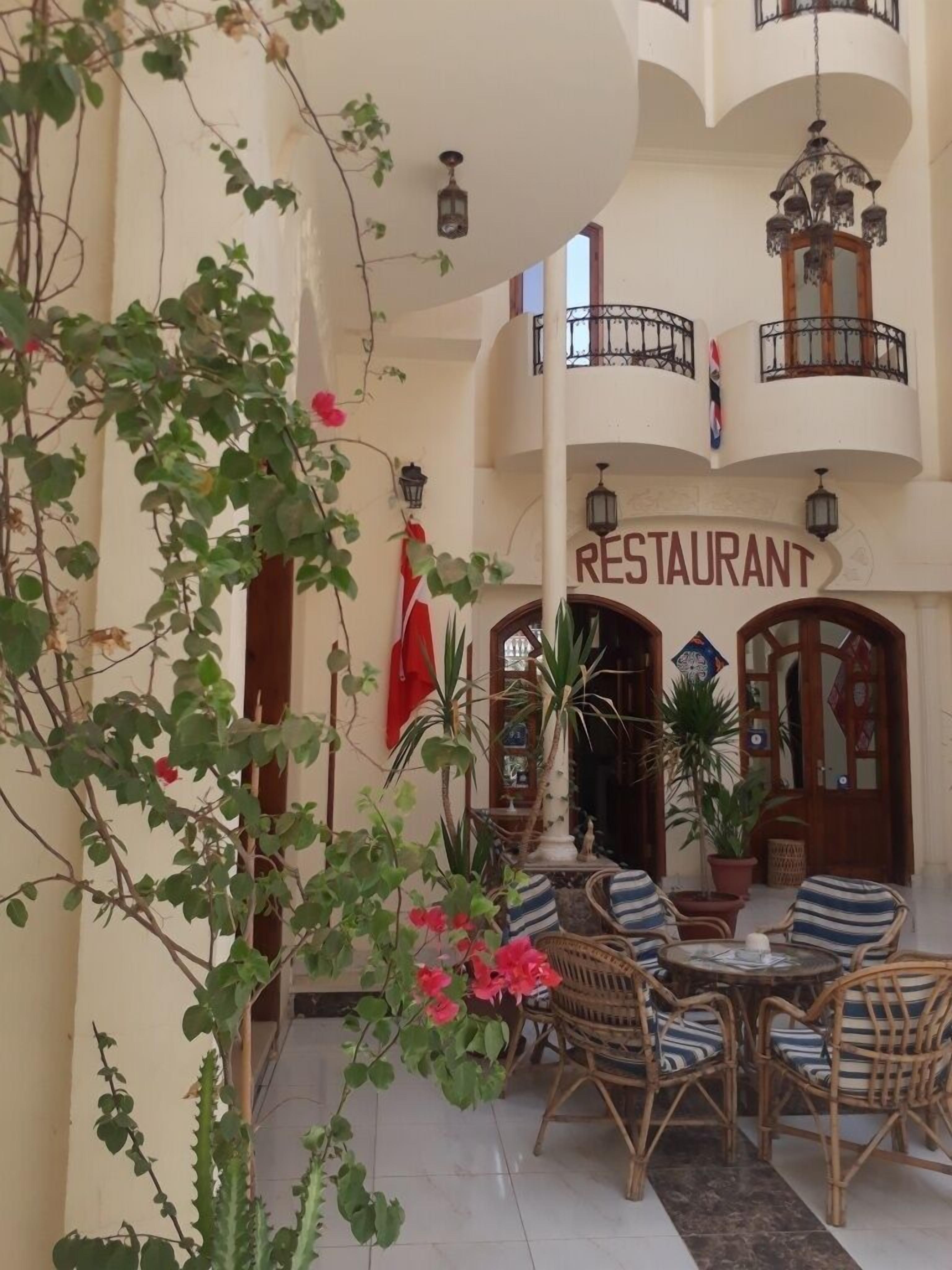 A restaurant with outdoor seating, surrounded by potted plants and a balcony.