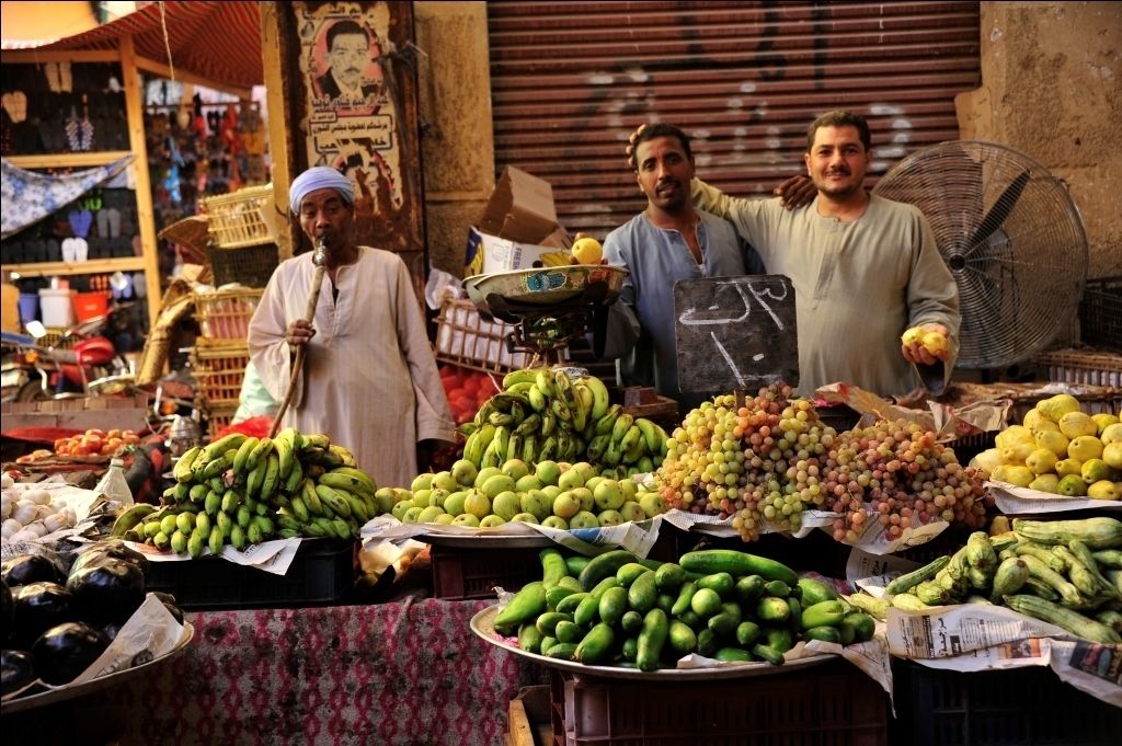 Un puesto de mercado con diversas frutas y verduras, como plátanos, uvas y limones.