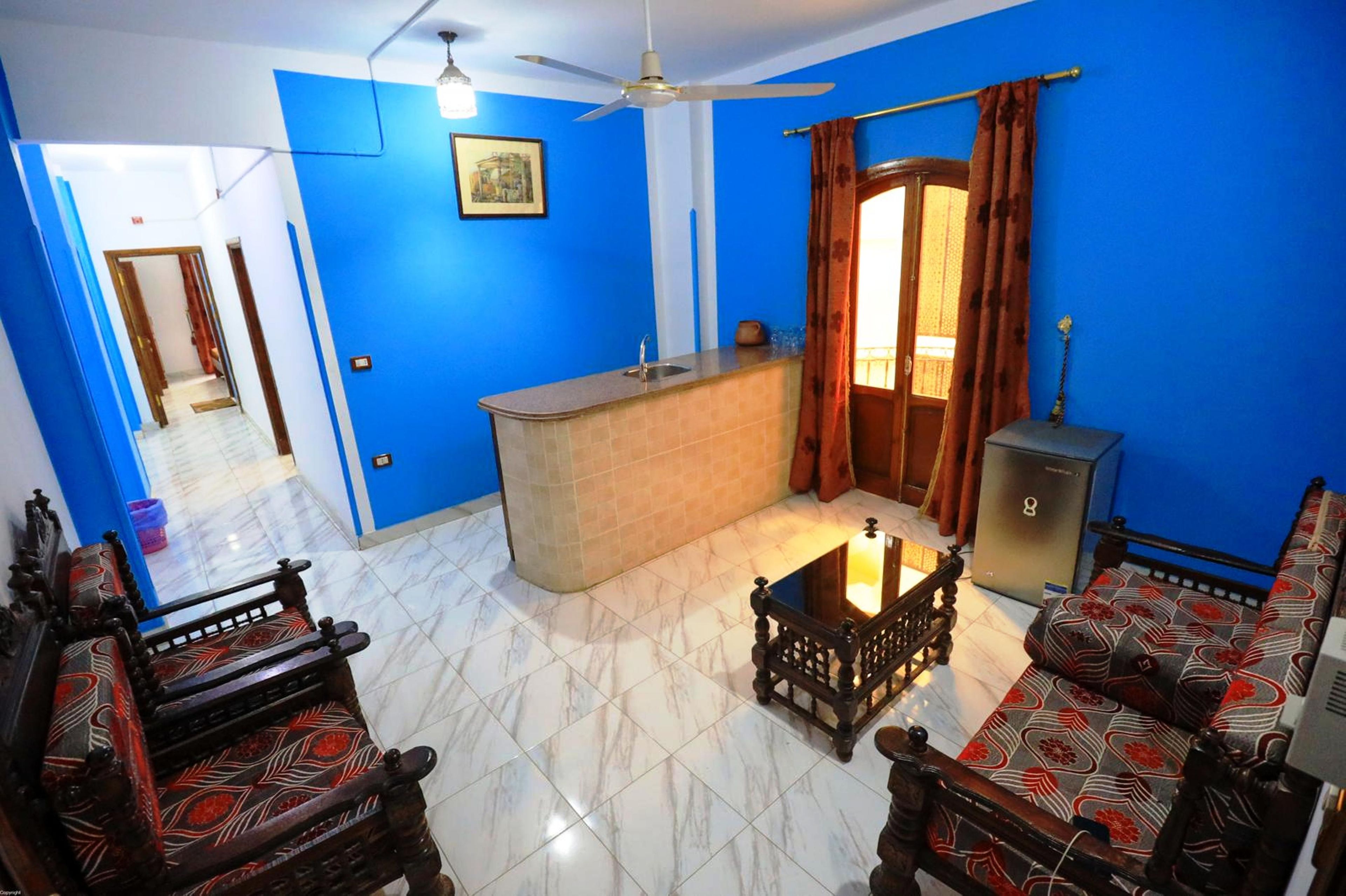 Una sala de estar con un sofá, una mesa de centro y un televisor. Hay una zona de cocina con un fregadero y un refrigerador.