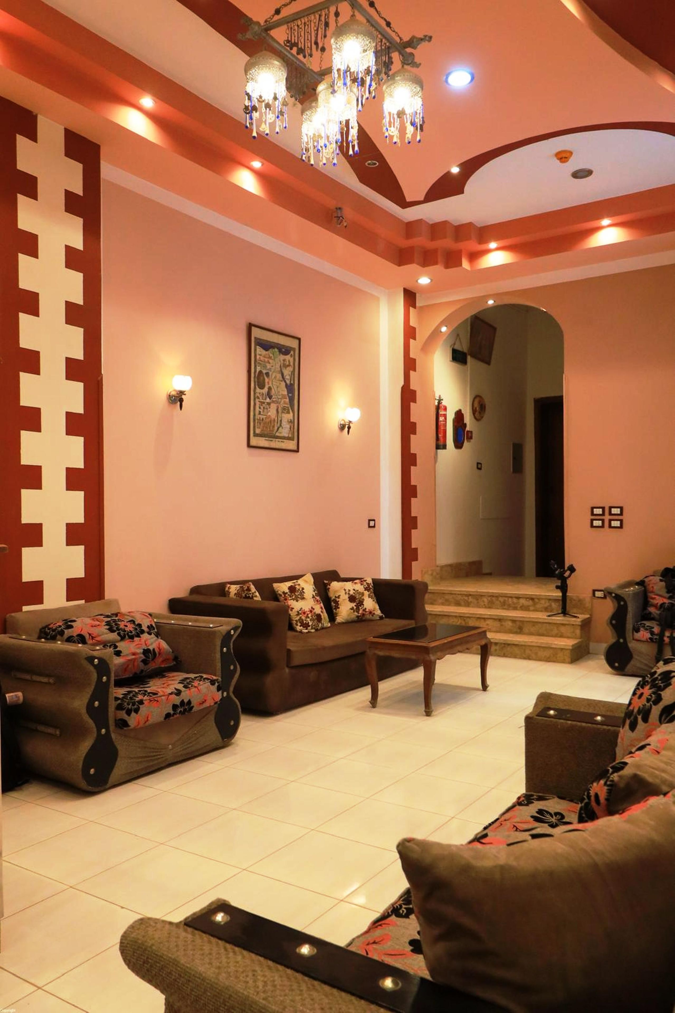 A living room with a sofa set, a coffee table, and a chandelier. There is a framed picture on the wall and a fire extinguisher mounted on the wall.