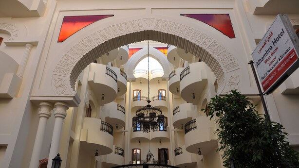 A hotel interior with multiple balconies, a central chandelier, and a sign indicating the hotel name and amenities.