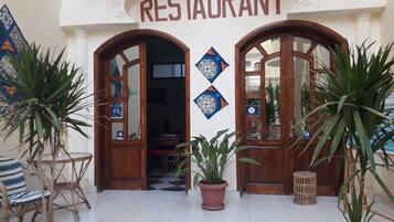 A restaurant entrance with two wooden doors, a tiled floor, and potted plants.