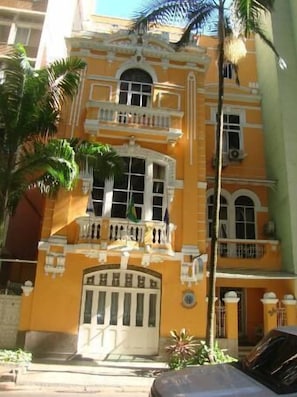 A yellow building with a central entrance, balconies, and palm trees. - Hotel Venezuela (Rio de Janeiro)