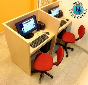 A hotel reception desk with two computer workstations, each with a keyboard and monitor, and red office chairs. - Hotel Venezuela (Rio de Janeiro)