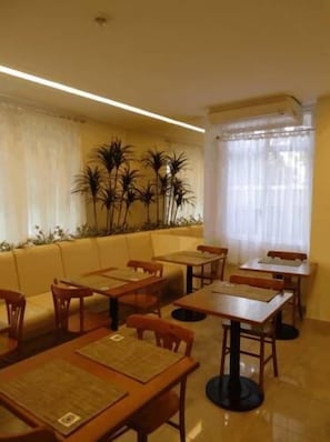 A restaurant with wooden tables and chairs, a yellow cushioned bench, and a wall of tall plants. - Hotel Venezuela (Rio de Janeiro)