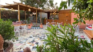 Ein Terrassenbereich im Freien mit gefliestem Boden, Holztischen und -stühlen sowie Blumentöpfen.