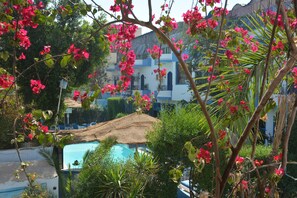 Un área de piscina con techo de paja, rodeada de exuberante follaje y flores rosadas.