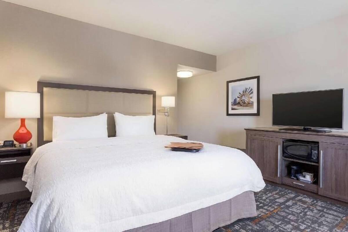 A hotel room with a large bed, a television, a desk with a lamp, and a framed picture on the wall.
