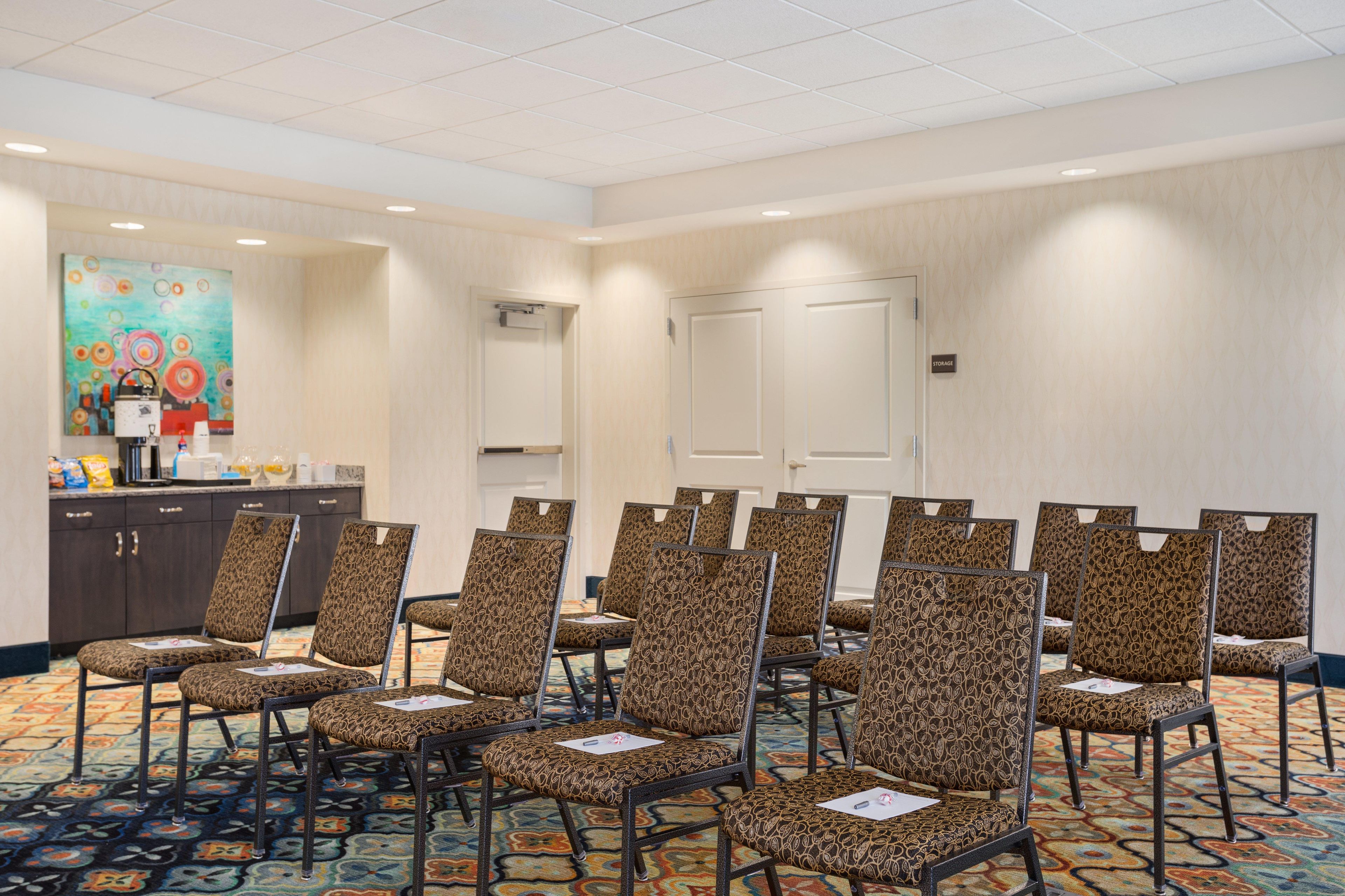 A conference room with patterned chairs, a carpeted floor, a painting on the wall, and a storage door.