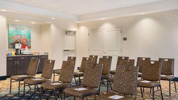 A conference room with patterned chairs, a carpeted floor, a painting on the wall, and a storage door.