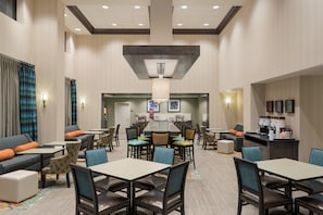 Un vestíbulo de hotel con varias zonas de estar, incluyendo sofás y mesas, una lámpara central y una estación de café.