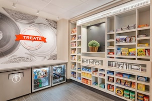 Una sección de snacks y artículos varios con una variedad de productos envasados y un refrigerador.