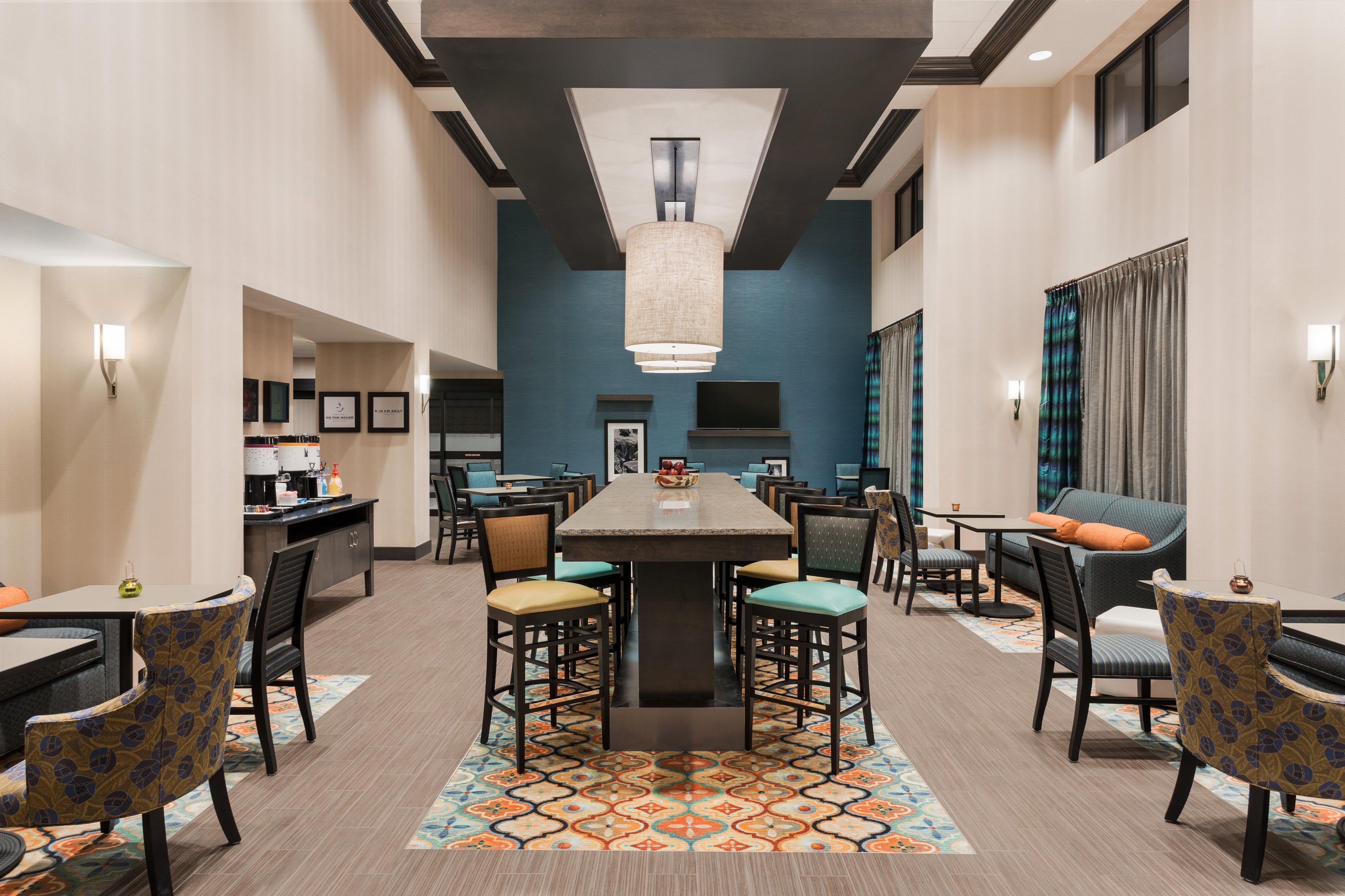 A hotel dining area with a central bar, multiple seating options, and a television screen.