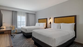 A hotel room with two beds, a desk, a chair, and a television.