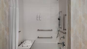 Un baño moderno con ducha a nivel, barras de apoyo, toallero y cabezal de ducha de mano.