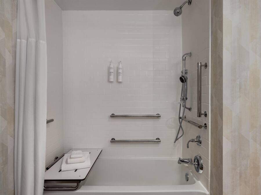 Un baño moderno con ducha a nivel, barras de apoyo, toallero y cabezal de ducha de mano.