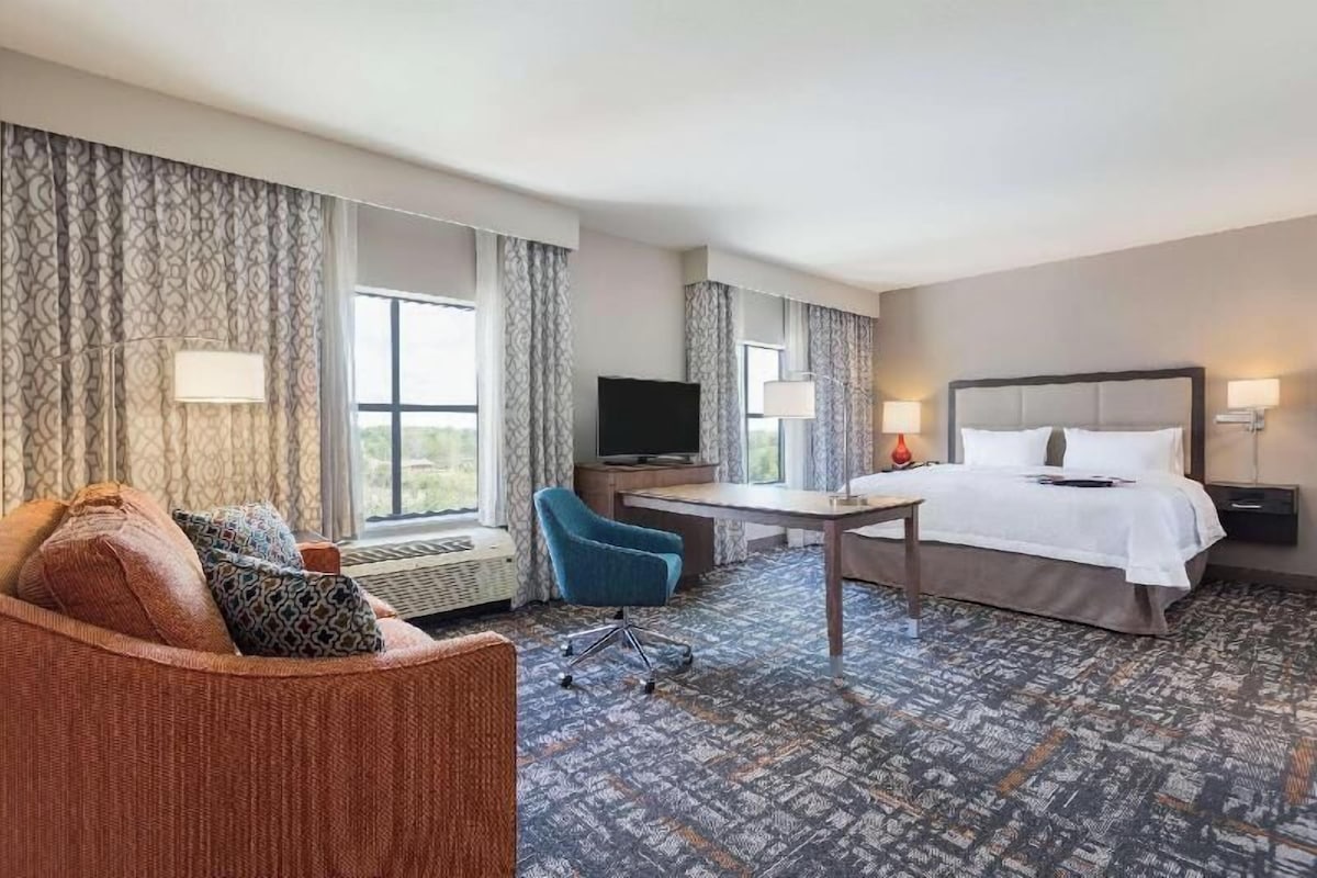 A hotel room with a bed, a desk, a chair, a television, and a large window.