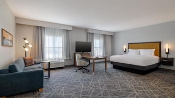 A hotel room with a bed, a desk, a television, a sofa, and a window with curtains.