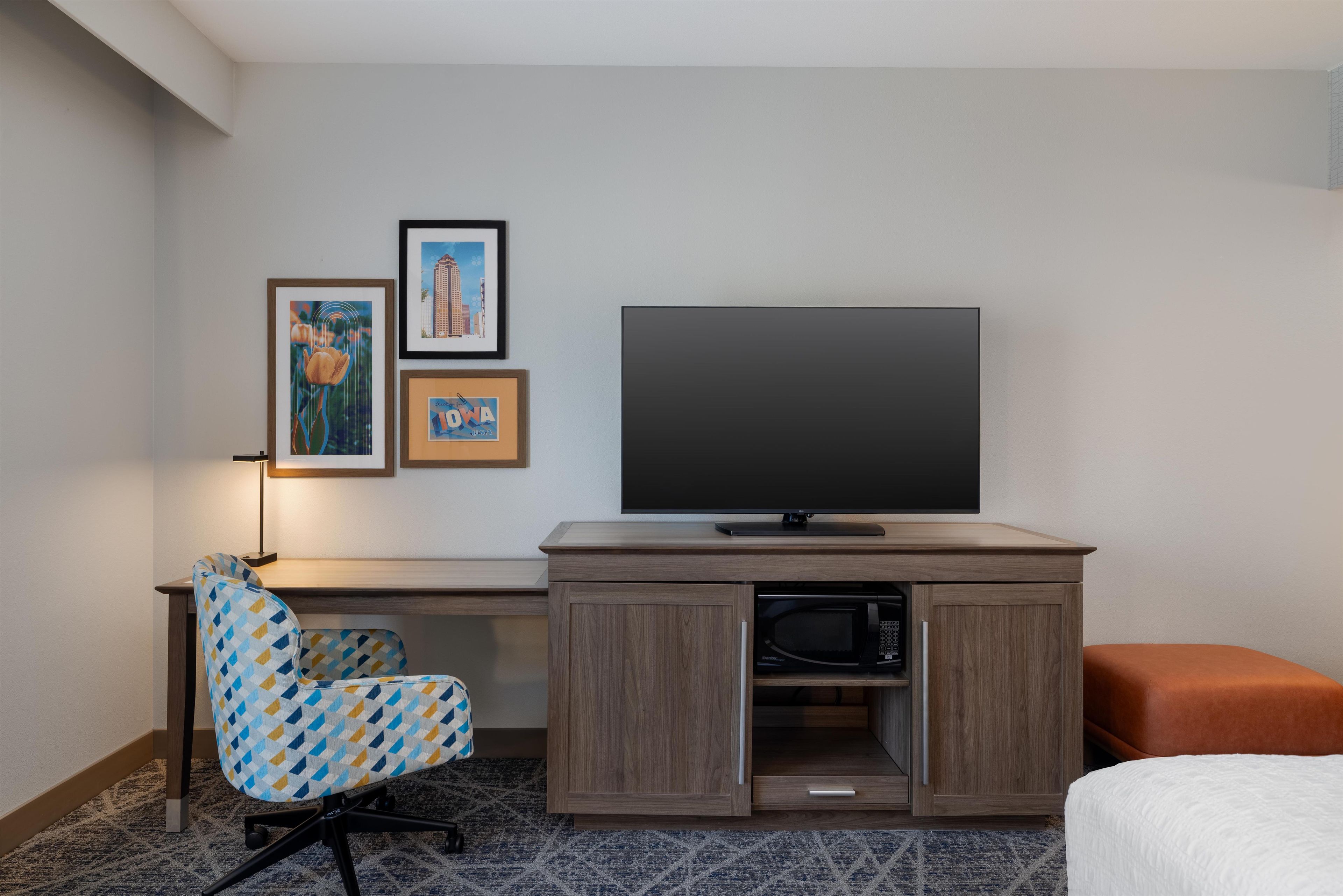 A hotel room with a TV, a desk with a chair, a microwave, and a bed.