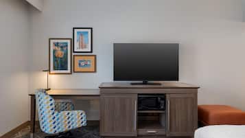 A hotel room with a TV, a desk with a chair, a microwave, and a bed.