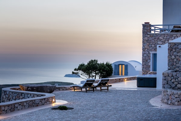 A stone pathway leading to a seating area with lounge chairs, a stone wall, and a view of the sea.