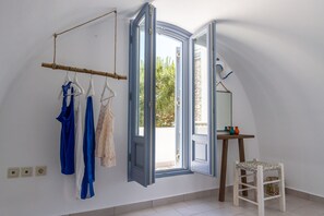 A room with a large open window, a wooden chair, and a clothing rack with various garments.
