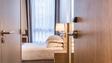 A hotel room with a wooden floor, a bed with white linens, a bedside table with a lamp, and a large mirror.