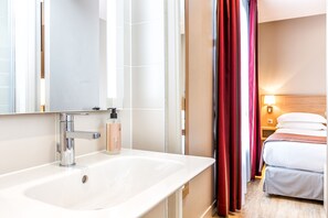 Ein Hotelbad mit einem weißen Waschbecken, einem Spiegel und einer Shampooflasche.