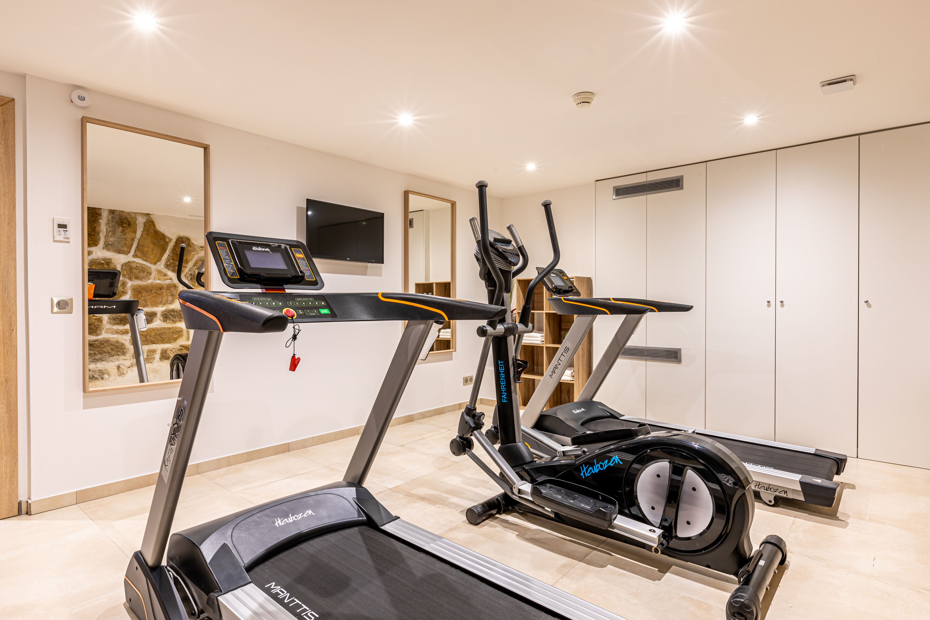 Een huisgymnasium met loopbanden, elliptische trainers en een hometrainer.