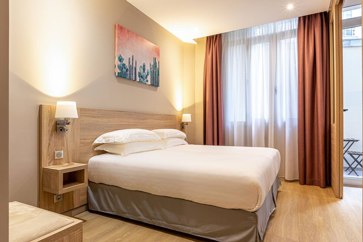 Habitación de hotel con una cama grande, lámparas de noche, una mesita de noche y un cuadro en la pared.