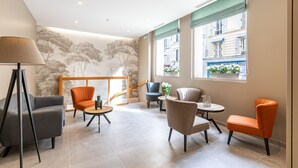 Un moderno vestíbulo de hotel con zona de estar, una escalera y grandes ventanales con vistas a la ciudad.