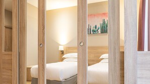 Una habitación de hotel con dos camas, paneles de madera, una mesita de noche con una lámpara y un cuadro en la pared.