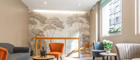 A modern hotel lobby with a seating area, a staircase, and a view of the building outside.