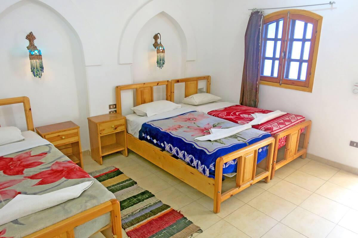 Un dormitorio con dos camas de madera, una mesita de noche, un aparador, una ventana con cortinas e iluminación empotrada en la pared.