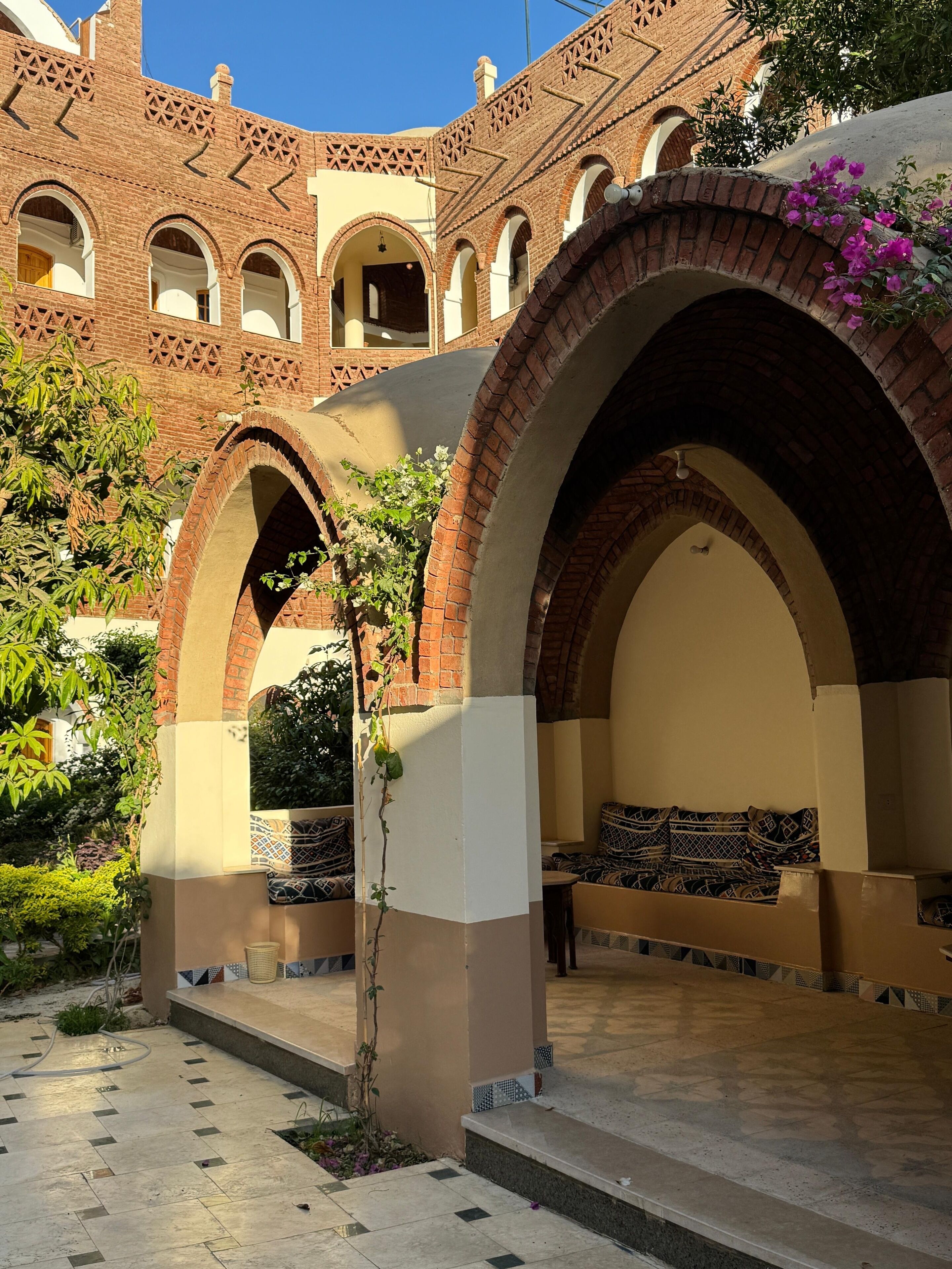 A courtyard with brick arches, a seating area with patterned cushions, and a tiled floor.