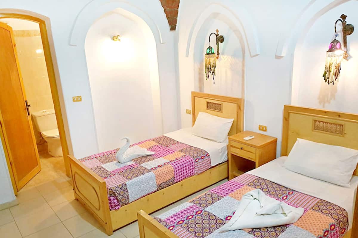 Una habitación de hotel con dos camas de madera, una mesita de noche de madera, una puerta de madera y un inodoro blanco.