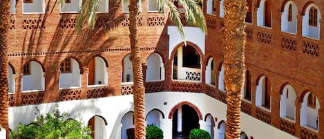 A courtyard with a brick building featuring arched windows and palm trees.