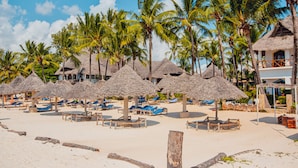 Een strand met rieten parasols, palmbomen en ligstoelen.