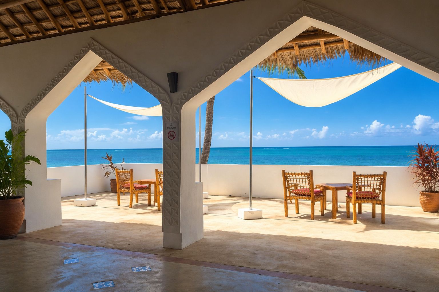 Un espacio de estar al aire libre cubierto con vista al océano, con sillas y mesas de madera y una estructura de techo de paja.