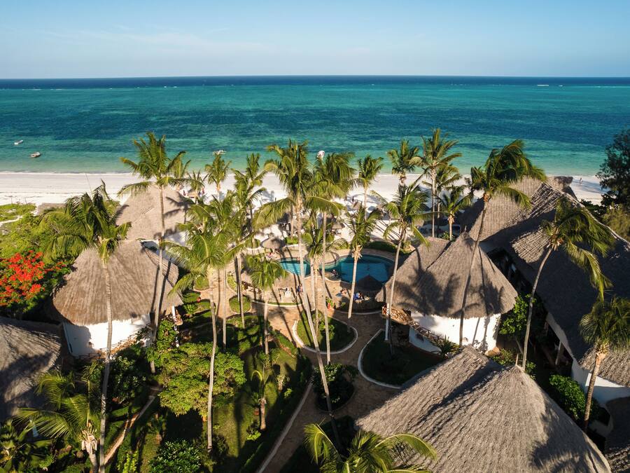 A resort with thatched-roof buildings, a pool, and a beach view.