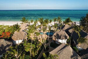 Un resort con edificios de techo de paja, una piscina y vista a la playa.