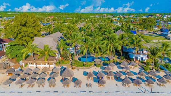 Un complexe hôtelier doté d’une piscine entourée de palmiers et agrémenté de parasols en chaume.
