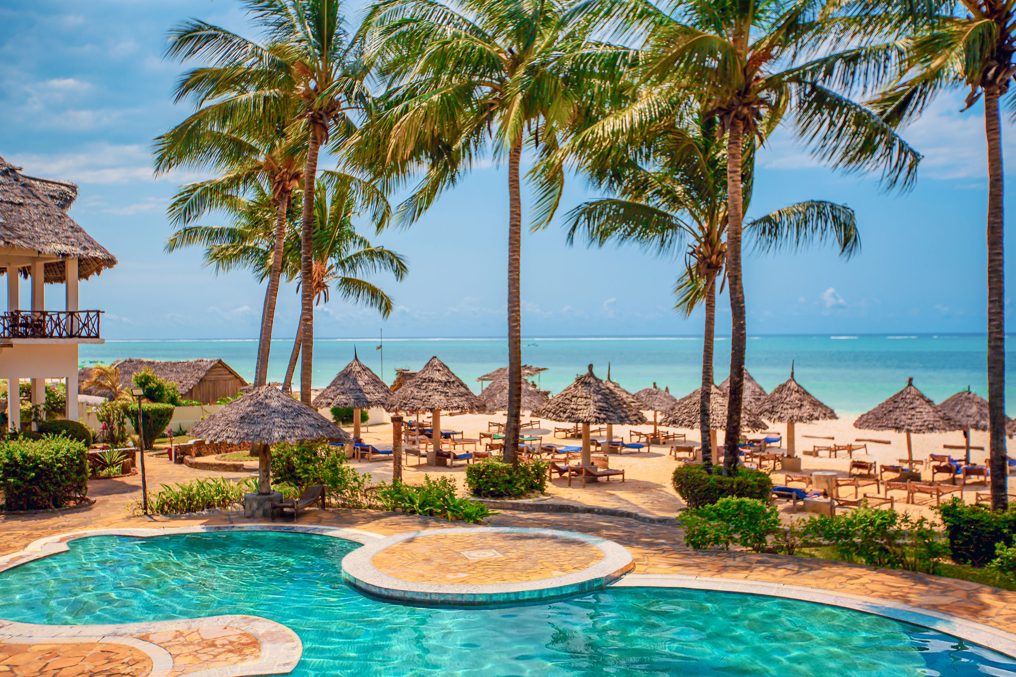 A pool area with a circular water feature, surrounded by palm trees and beach chairs.